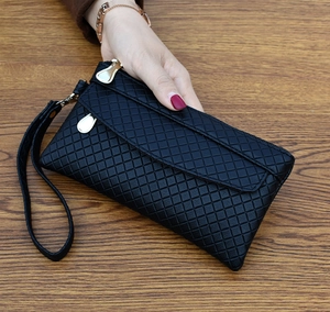 Detail of black quilted envelope clutch with gold zipper and wrist strap on wood surface
