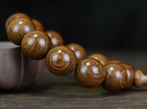 Macro detail of natural sandalwood beads with golden silk grain and rustic teapot decor