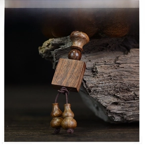 Macro detail of sandalwood beads with square pendant and twin gourds on rustic wood