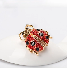 Detailed close-up of a ladybug brooch with red and black rhinestones on a ceramic spoon
