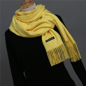 Close-up of vibrant yellow cashmere scarf with fringe details and woven brand tag