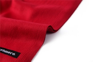 Close-up of red cashmere scarf showing soft knitted texture and woven logo tag