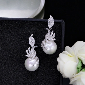 Close-up of pearl drop earrings with sparkling zircon wing design on black jewelry display