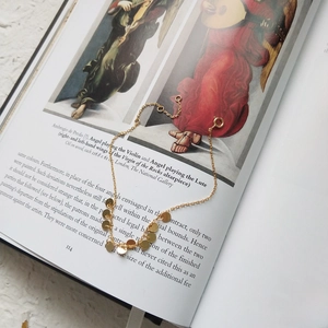 Detail of gold chain bracelet with round disc charms on an artistic book background