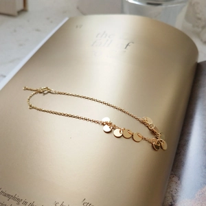 Detail of a minimalist gold bracelet with polished circular charms on an artistic book