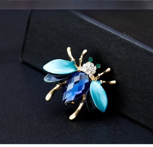 Macro shot of beetle brooch with blue teardrop gemstone and gradient enamel details
