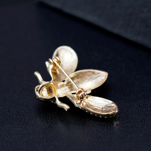 Elegant gold bee brooch with textured wings and oil-painted details on dark leather