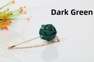Detail of dark green satin rose brooch with gold chain and leaf on white surface