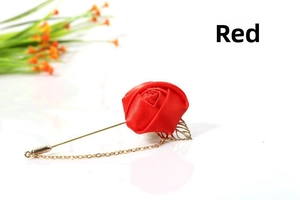 Detail of red satin rose brooch with gold chain and leaf charm on white surface