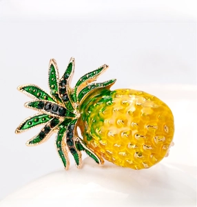 Detail of yellow enamel pineapple brooch with green crystals on white ceramic surface
