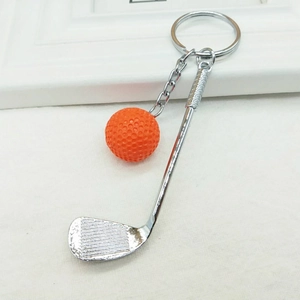Detail view of silver golf club keychain with orange mini ball on white textured surface