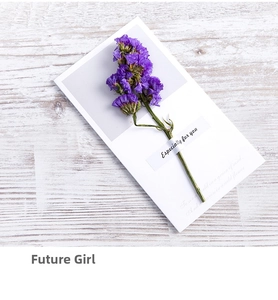Close-up of a white gift card with purple dried flowers on a light wood background