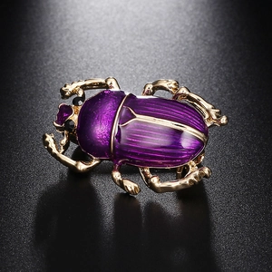 Détail d'une broche scarabée violette avec pattes dorées sur fond sombre texturé