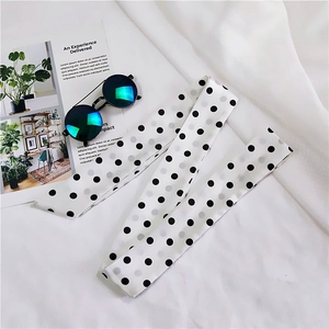 Detailed view of long white polka dot scarf styled with sunglasses and magazine on white fabric