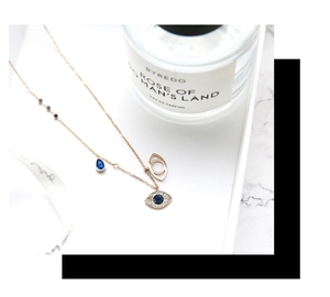 Close-up of rose gold Evil Eye necklace with blue crystals on marble surface