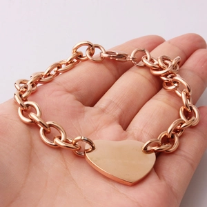 Detail view of rose gold stainless steel link chain bracelet with heart charm held by hand