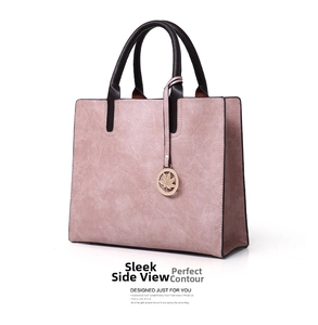 Detail of dusty rose tote bag featuring dark brown handles and golden maple leaf charm