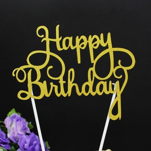 Macro shot of glittery gold Happy Birthday cake topper with cursive font on black background