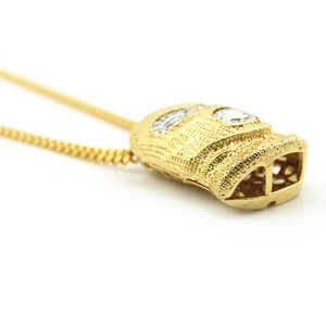 Close-up of hip hop pendant with gold mask design and clear gemstone eyes on a chain