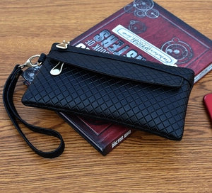 Close-up of black quilted PU leather clutch with gold zipper and wristlet on wood surface