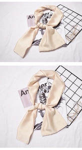 Detail of a beige silk-feel skinny scarf knotted on a stylish white fabric background