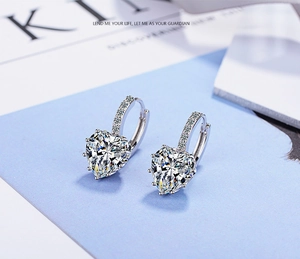 Macro detail of silver heart-shaped zircon earrings with pavé stones on blue card