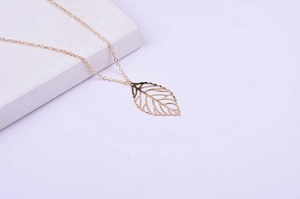 Detailed close-up of rose gold leaf pendant on a minimalist chain displayed on white stand