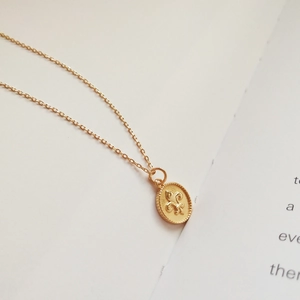 Close-up of golden 925 silver Fleur-de-lis oval pendant on a minimalist book background