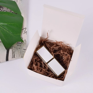 Top view of white gift box with brown raffia paper filler and gold-trimmed item