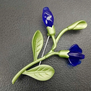 Detail of violet flower brooch with green enamel leaves and blue freshwater pearl accents