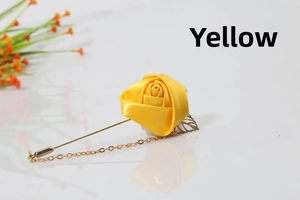 Detailed close-up of yellow satin rose brooch with gold chain and leaf on white surface