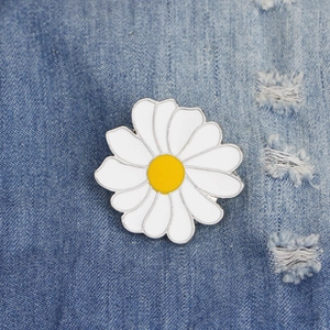 Detail of a white enamel daisy brooch with yellow center on blue denim fabric