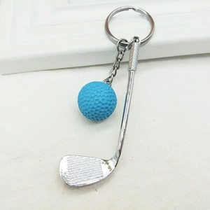 Detail of blue golf ball keychain with silver metal club on white textured fabric