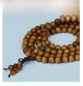 Close-up of 108 sandalwood prayer beads with natural wood grain and a black knot decor