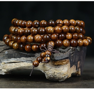 Macro detail of dark brown wooden prayer beads on aged wood, showing natural grain texture