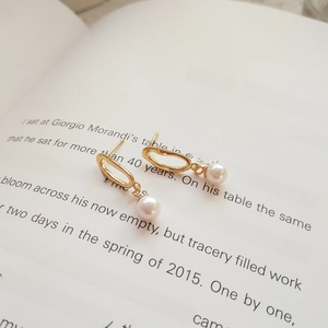 Detailed view of gold irregular oval pearl earrings placed on minimalist book pages