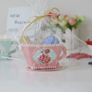 Pink teacup-shaped gift box with rose patterns and golden ribbon in clear packaging
