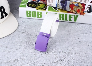 Detail view of a white nylon canvas belt with a matte purple buckle on a textured floor