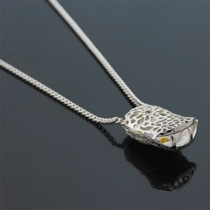 Detail view of a silver hip hop pendant with a hollow cage design and a yellow gemstone