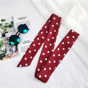 Polka dot long silk scarf in red and white laid on white fabric with fashion props