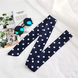 Detailed view of long navy blue polka dot silk scarf styled with sunglasses and magazine