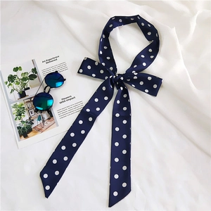 Navy blue polka dot silk scarf tied in a bow next to stylish sunglasses on white fabric