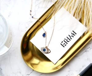 Detail of rose gold evil eye necklace with blue crystals on a decorative golden tray