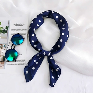 Navy blue polka dot silk scarf tied on white fabric with sunglasses and magazine