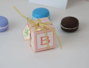 Close-up of pink baby cube gift box with gold ribbon and decorative letter B detail