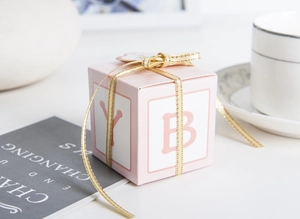 Pink square party favor box with gold ribbon and elegant letter design detail