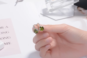 Close-up of olive green zircon earrings with silver hooks held for size reference