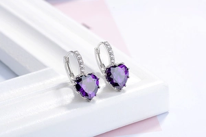 Macro shot of silver earrings with purple heart-shaped gemstones and pave stones