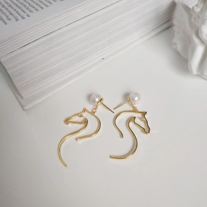 Detail of 925 silver horse head stud earrings with pearl and golden finish on a book