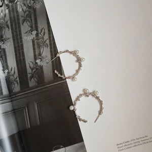 Detailed close-up of 925 sterling silver hoop earrings with white pearls on a magazine